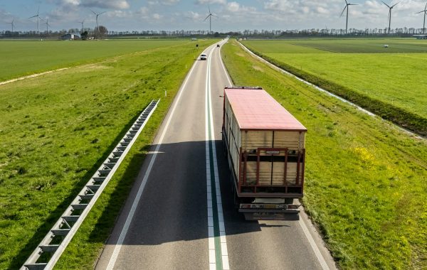 Camion che percorre una strada tra campi e turbine eoliche, simbolo del trasporto merci autonomo ed elettrico