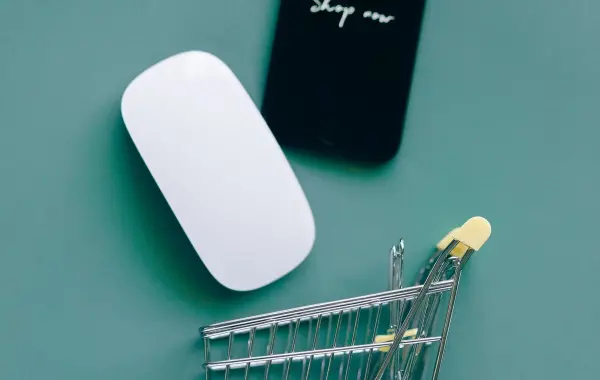 Smartphone appoggiato su un piccolo carrello della spesa, simbolo degli acquisti online tramite assistenti AI