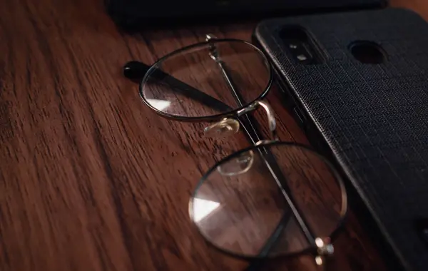 Occhiali e smartphone appoggiati su un tavolo di legno, simbolo degli occhiali smart con assistente AI