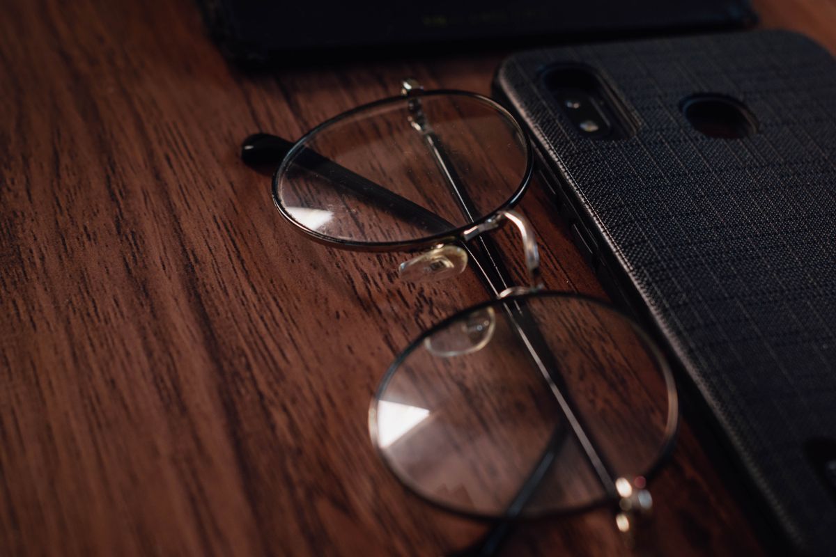 Occhiali e smartphone appoggiati su un tavolo di legno, simbolo degli occhiali smart con assistente AI