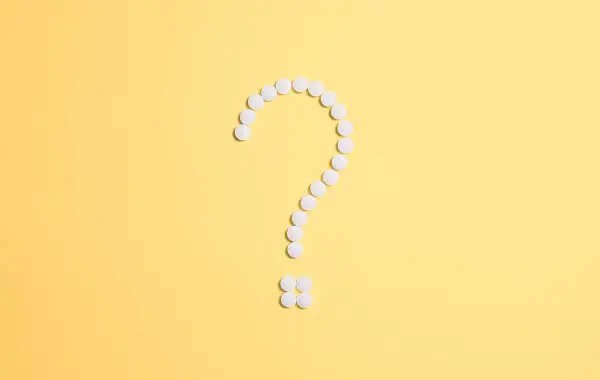 Punto interrogativo formato da pillole bianche su sfondo giallo