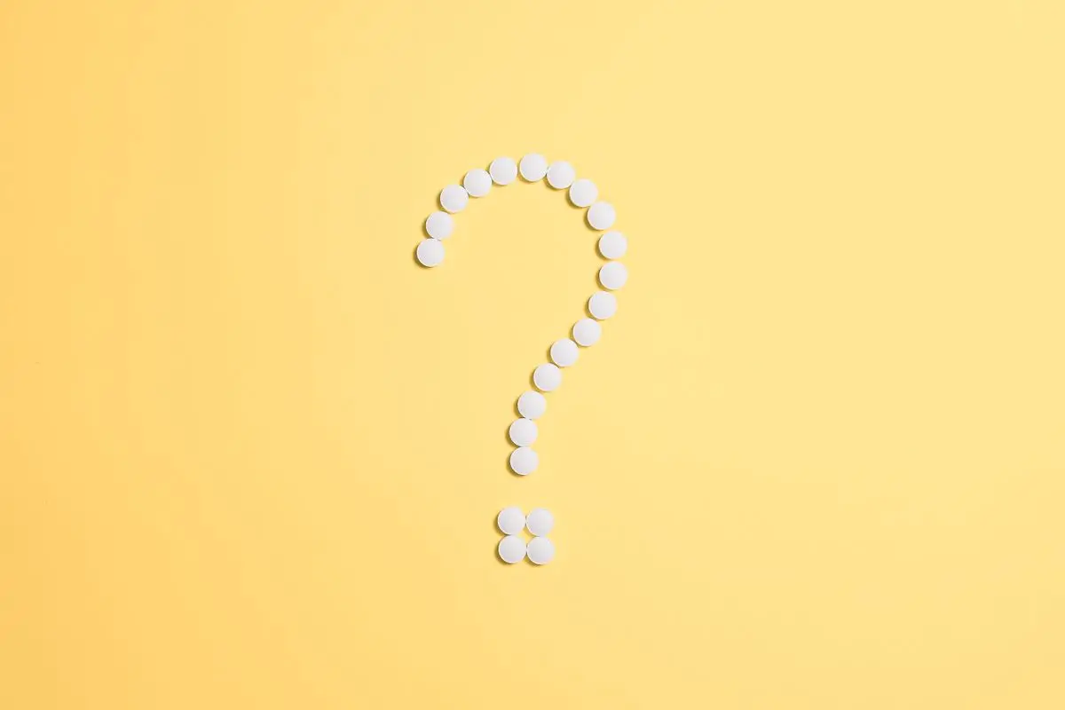 Punto interrogativo formato da pillole bianche su sfondo giallo